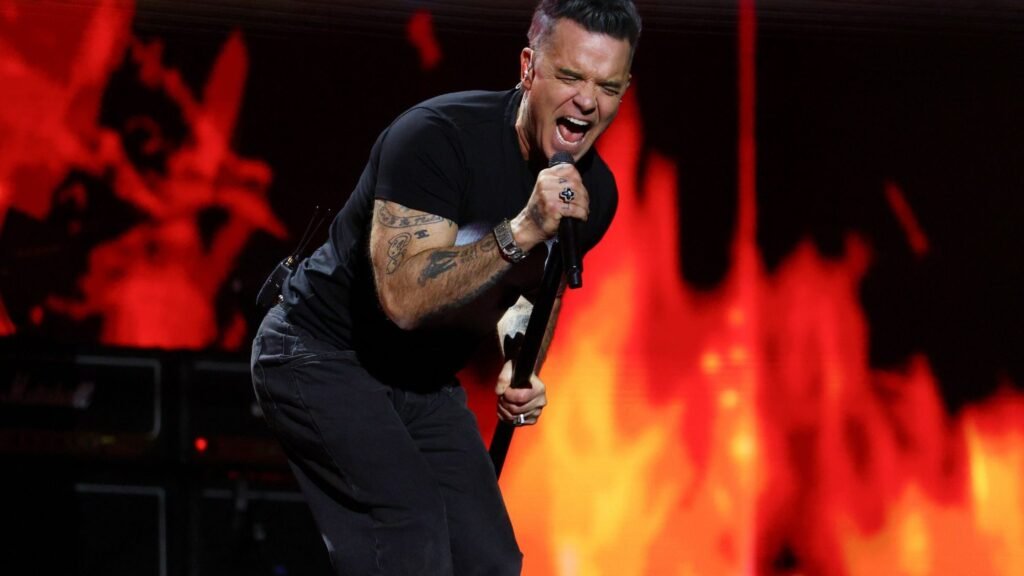 Robbie Williams. Crédito: performs on stage in 2026. JMEnternational/Getty Images.